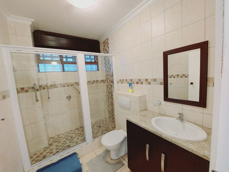A functional bathroom featuring a walk-in shower with glass enclosure, wall-mounted toilet, and a vanity cabinet with a granite countertop.