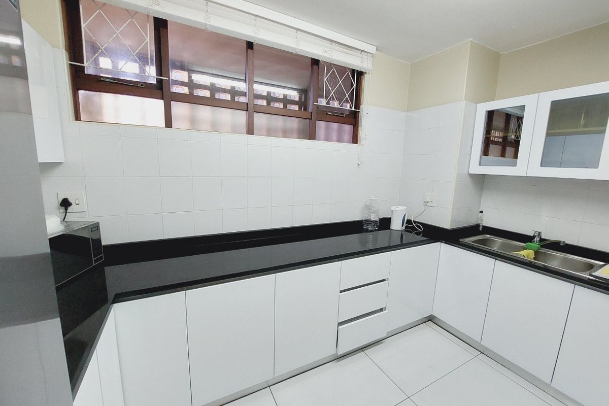 A clean, functional kitchen featuring white cabinetry, black granite countertops, tiled backsplash, and a stainless steel sink with natural light from the window.