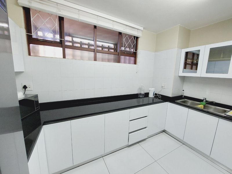 A clean, functional kitchen featuring white cabinetry, black granite countertops, tiled backsplash, and a stainless steel sink with natural light from the window.