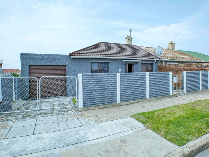 Front exterior view of a single-story house featuring a garage, secure boundary walling, and a paved driveway.