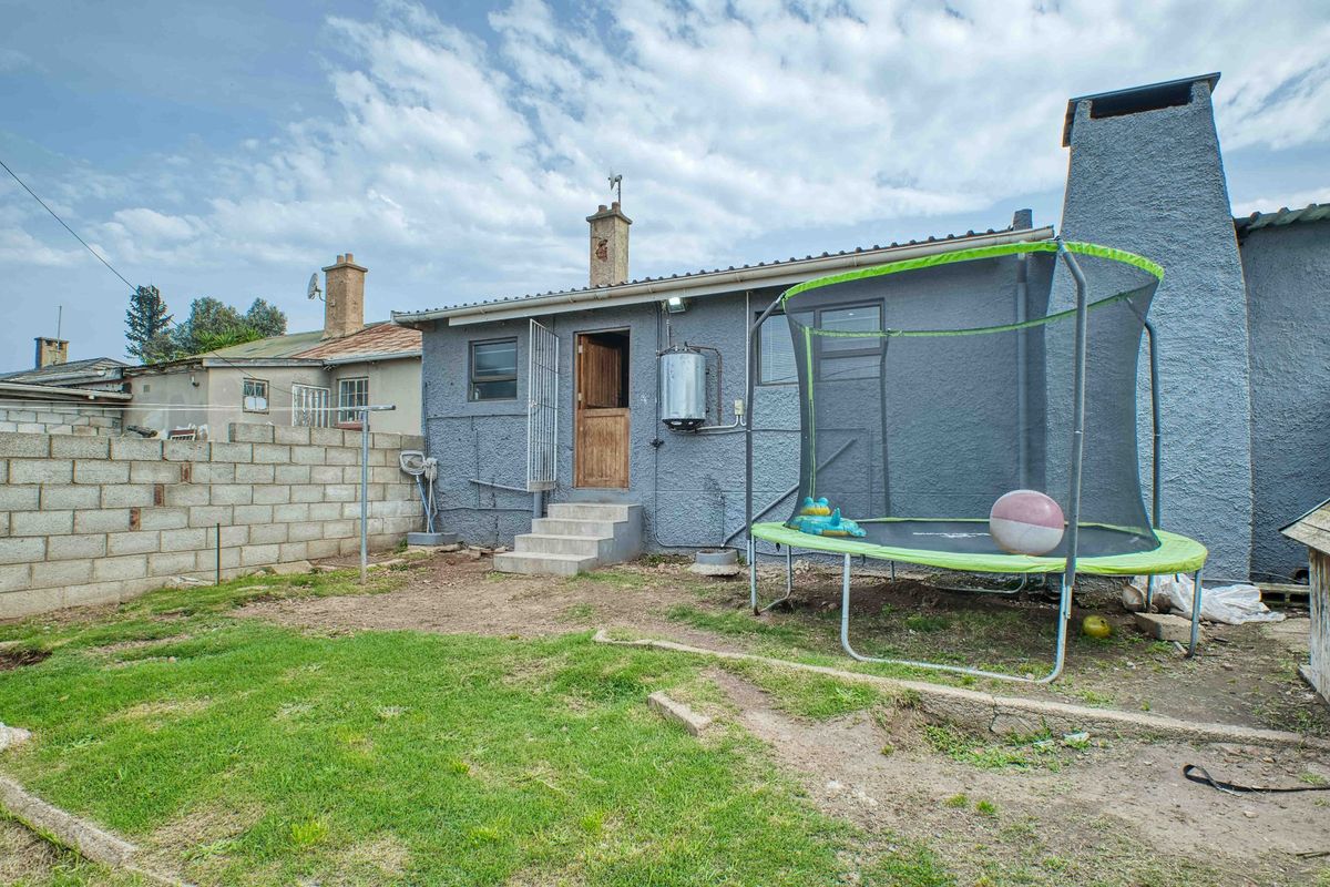 Rear exterior view of the property featuring a concrete block boundary wall, external chimney, and access steps leading to the back entrance.