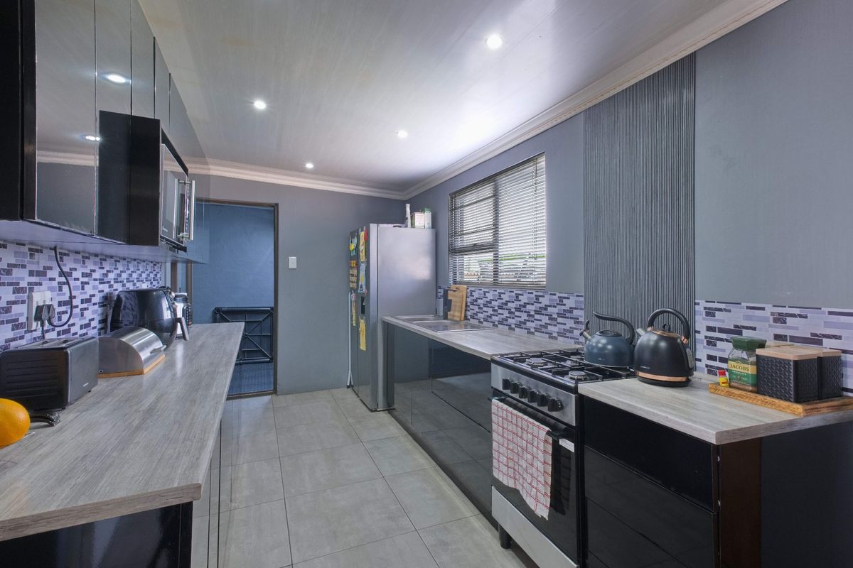 Modern galley-style kitchen featuring dark high-gloss cabinetry, wood-look laminate countertops, mosaic tile backsplash, and a gas stove.