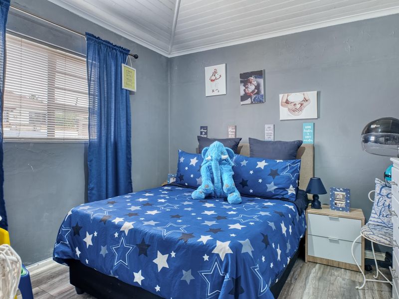 A bedroom featuring timber-look laminate flooring, a tongue and groove ceiling, and venetian blinds, providing a functional space with neutral wall finishes.