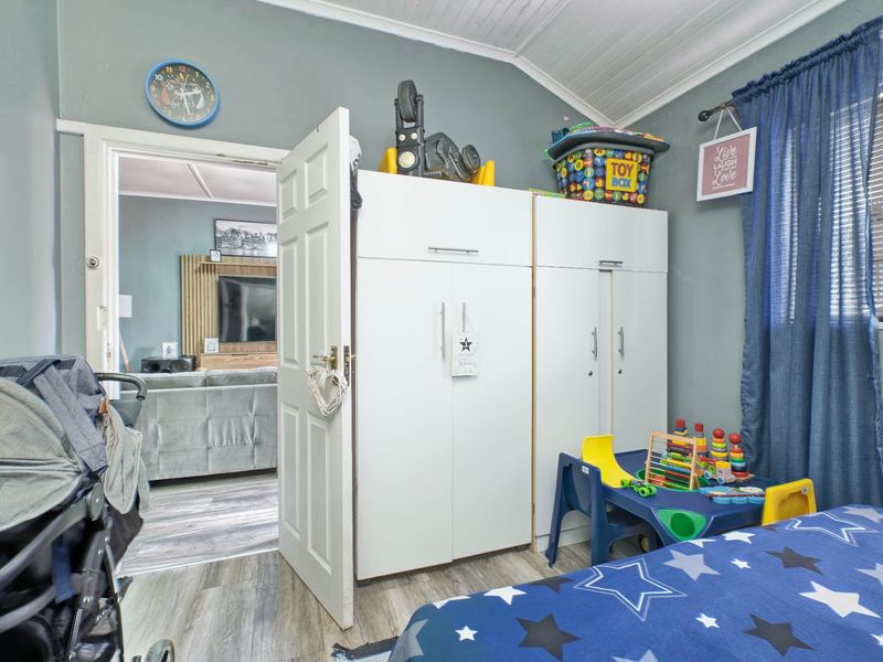A bedroom featuring built-in cupboards, timber-look laminate flooring, and a classic tongue and groove ceiling, with an open doorway leading to the living area.