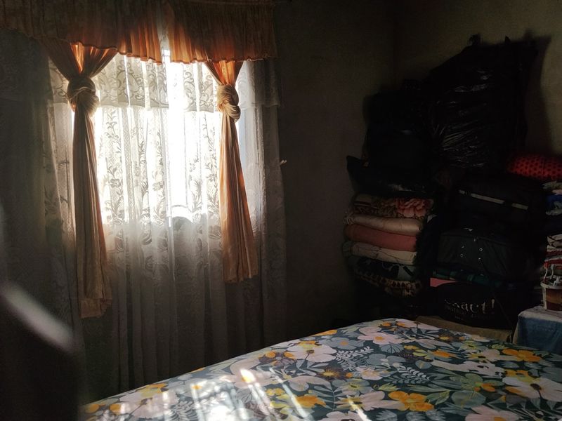 A dimly lit bedroom interior featuring a window with curtains, showing limited architectural detail due to poor lighting and clutter.
