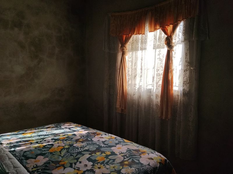 A bedroom featuring natural light through a window, with textured wall finishes requiring cosmetic attention.