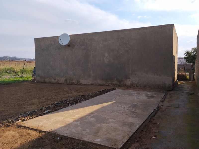 Rear exterior view showing a large plastered wall, a satellite dish, and a concrete slab set against an unfinished yard area.
