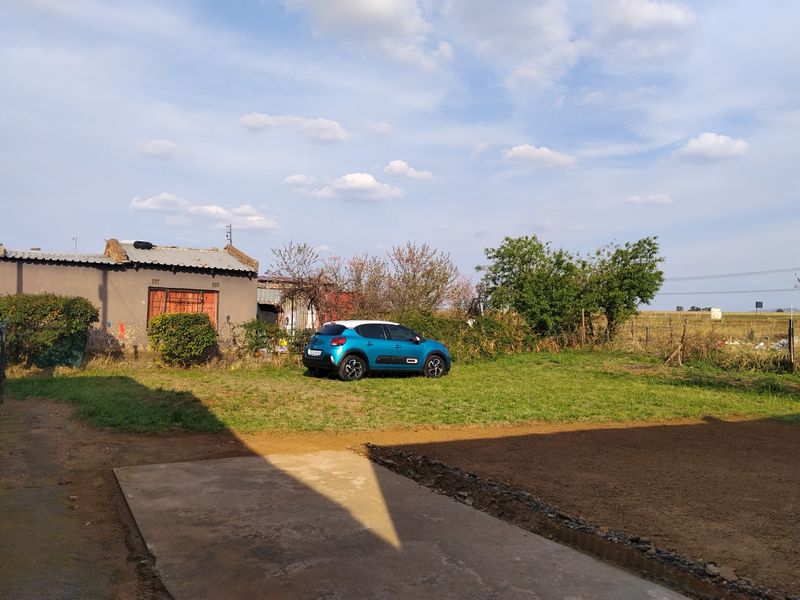 A view of the rear yard featuring a concrete driveway, open lawn area, and the rear elevation of the property structure.