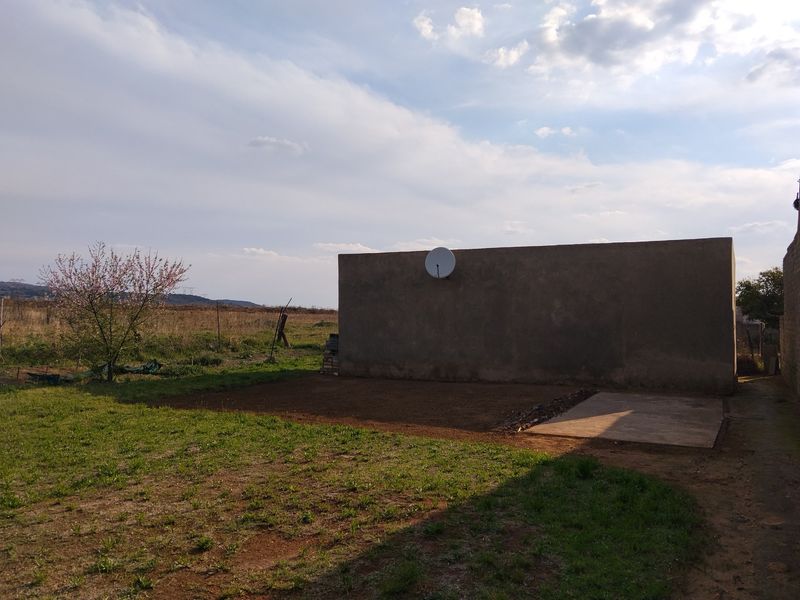 A view of the rear exterior wall of the property featuring a satellite dish and a small concrete patio area set against a garden.