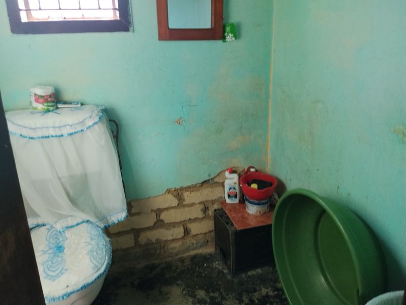A small bathroom featuring a toilet, with significant wall plaster damage and exposed brickwork requiring repair and renovation.