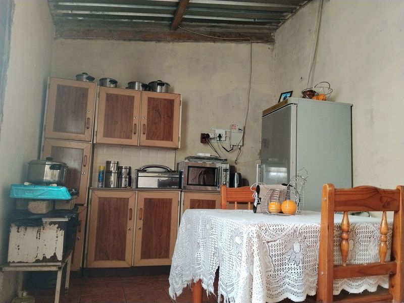 A compact kitchen area featuring built-in wooden cabinetry, tiled floors, and an exposed ceiling, requiring significant cosmetic updates and infrastructure improvements.