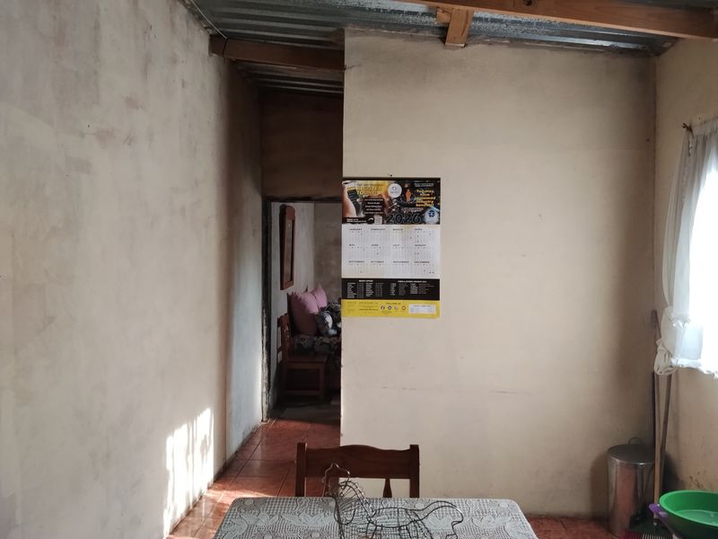 A basic living area featuring tiled flooring and an exposed corrugated metal ceiling, requiring cosmetic updates to improve the overall finish.