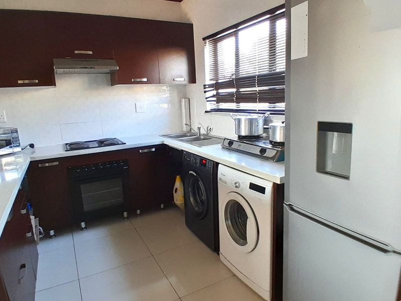 A functional kitchen featuring dark wood cabinetry, built-in oven and hob, extractor fan, double sink, and tiled flooring with space for laundry appliances.