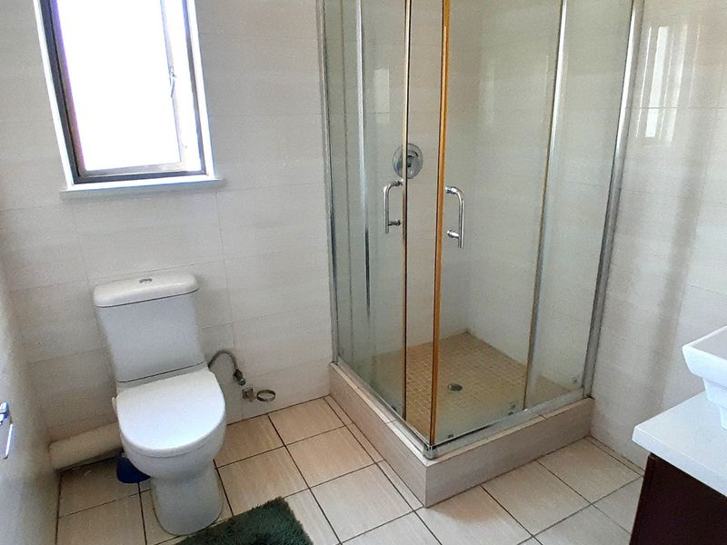 A functional bathroom featuring a glass shower enclosure, a standard toilet, and neutral tiled finishes throughout.