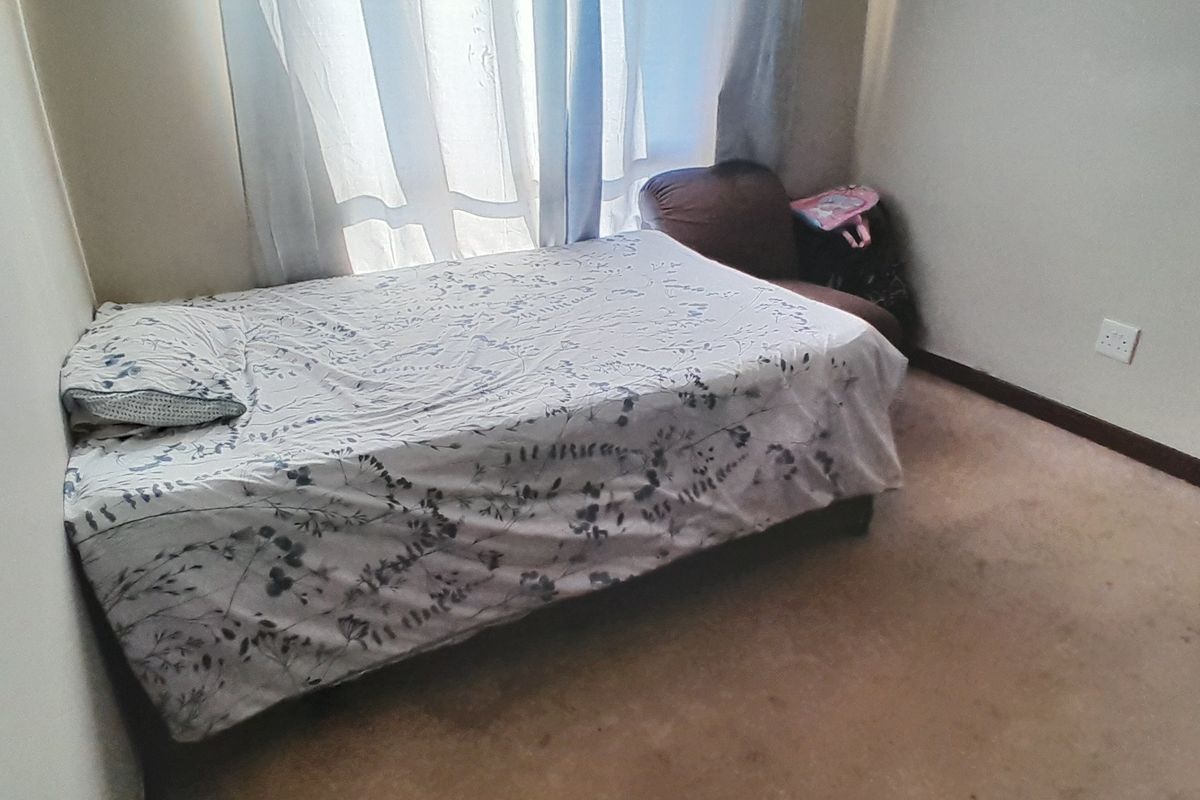 A compact bedroom featuring carpeted flooring and a window with curtains, providing a functional space for rest.