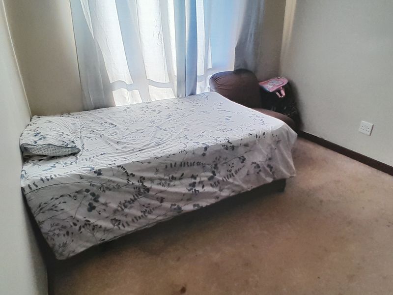 A compact bedroom featuring carpeted flooring and a window with curtains, providing a functional space for rest.