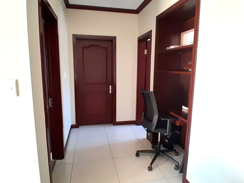 A hallway featuring tiled flooring, dark wood door frames, and a built-in desk area with integrated shelving.