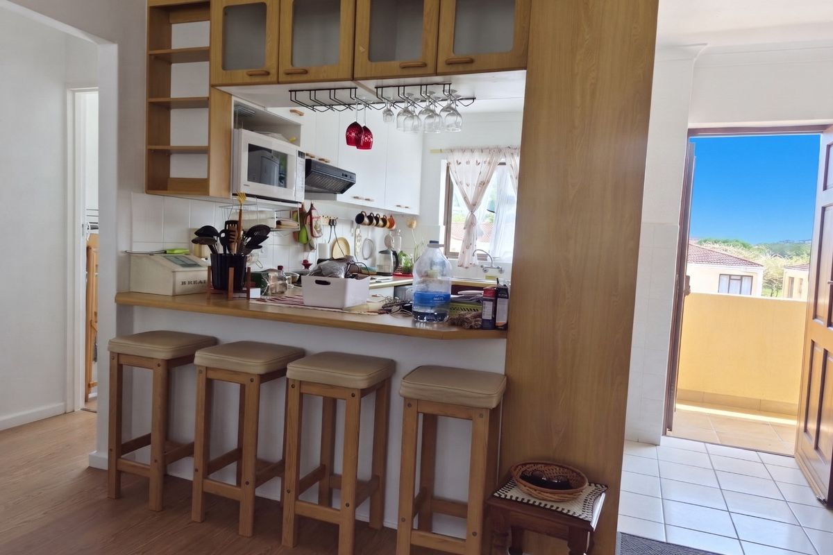 A functional kitchen featuring a breakfast bar, built-in cabinetry, and integrated appliances, with direct access to an outdoor balcony area.