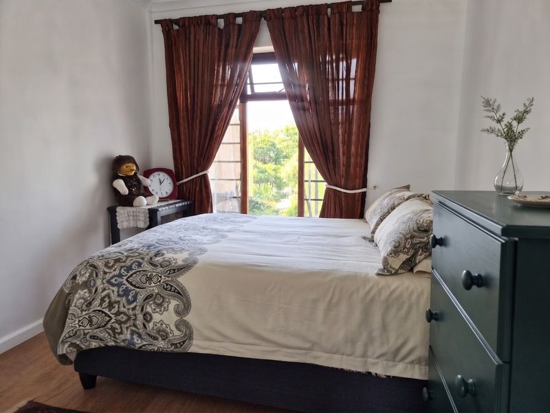 A cozy bedroom featuring laminate flooring and a window with natural light, offering a pleasant view of the surrounding greenery.