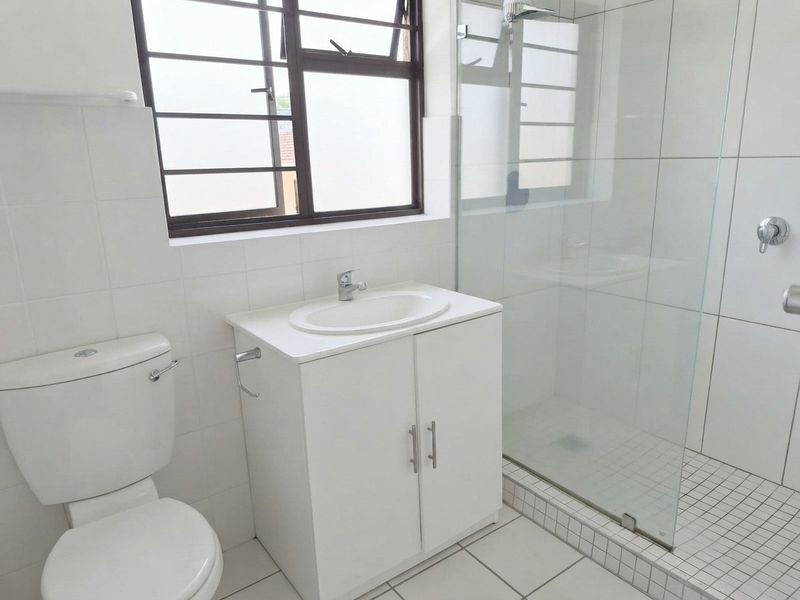 A clean, functional bathroom featuring a white vanity with basin, a toilet, and a glass-enclosed shower with tiled finishes throughout.