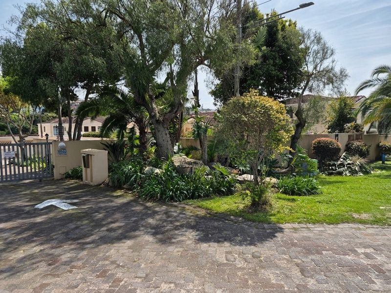 Front entrance view of the apartment complex featuring a paved driveway, secure metal gate, and established landscaped garden area.