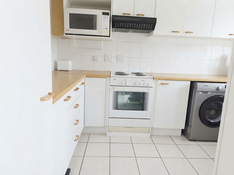 A functional kitchen featuring white cabinetry, light wood-tone countertops, tiled backsplash, and integrated appliances including a stove, extractor fan, and microwave.