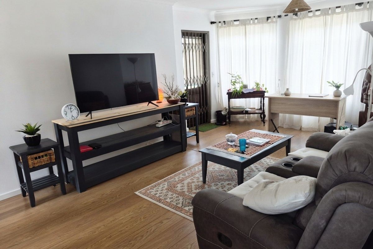 A well-lit living room featuring light-toned laminate flooring, neutral walls, and a security gate leading to an outdoor area.