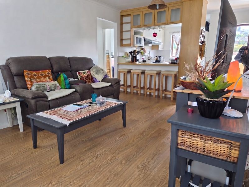 Open-plan living and kitchen area featuring wood-look laminate flooring, a breakfast bar, and functional kitchen cabinetry with integrated appliances.