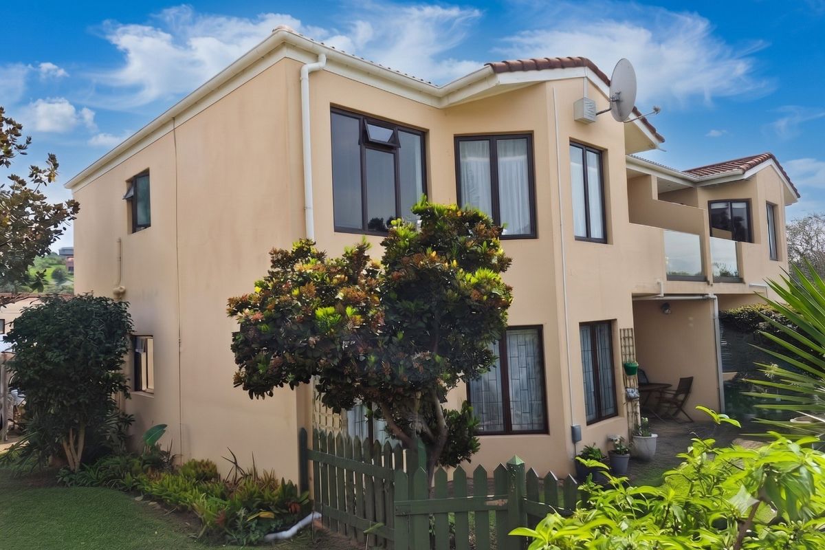 Rear view of a two-story apartment building featuring a paved patio, balcony with glass balustrade, and well-maintained exterior walls with aluminium window frames.