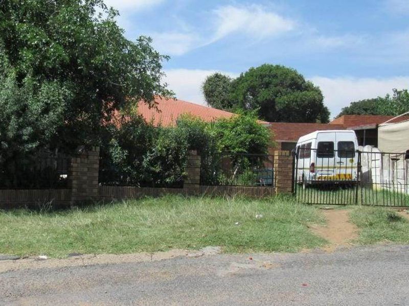 Front view of the property featuring a brick boundary wall, metal entrance gate, and a shade cloth carport structure.