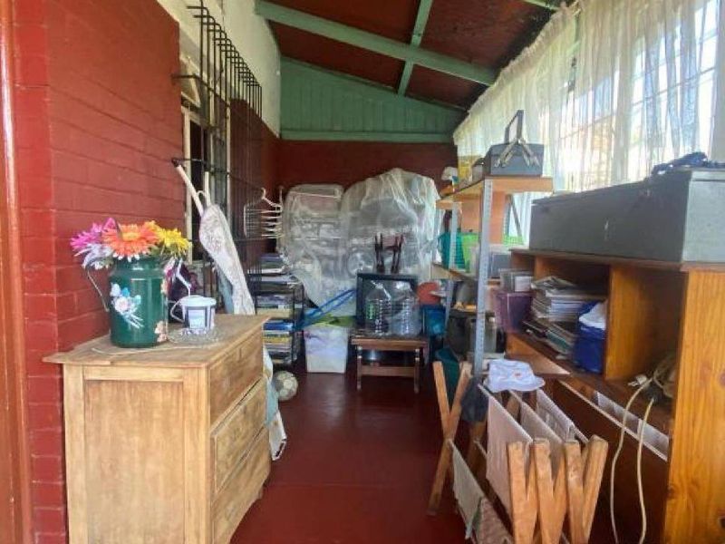 A covered patio area featuring exposed timber rafters, painted brick walls, and concrete flooring, currently utilized as a storage space.