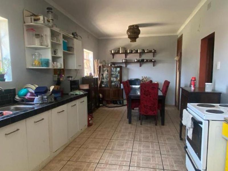 Open-plan kitchen and dining area featuring tiled flooring, built-in cabinetry, and a tiled backsplash, offering a functional layout with potential for modernization.