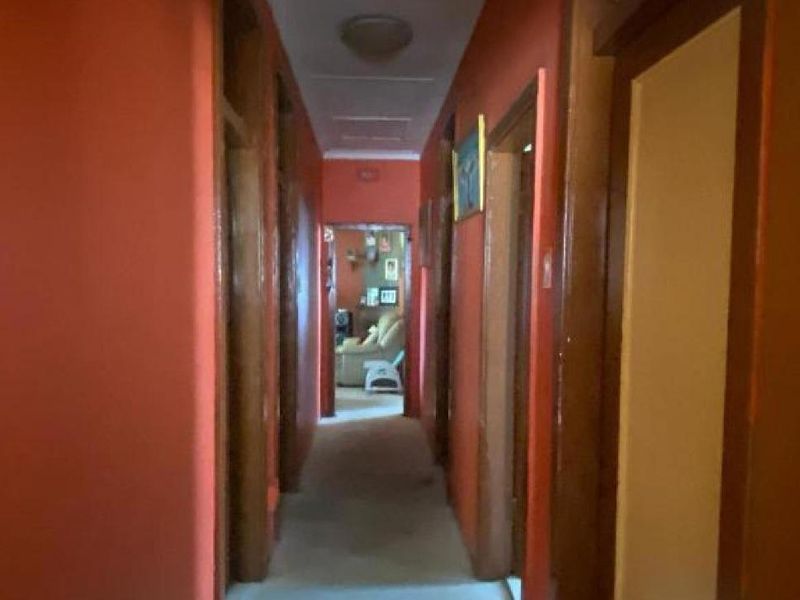 A narrow residential hallway featuring wooden door frames and dated wall paint, providing access to multiple rooms.