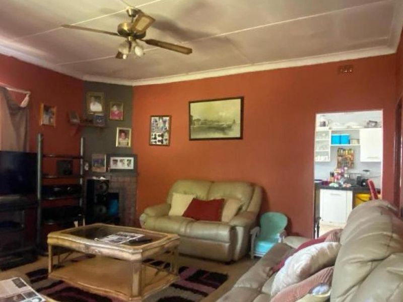 A living room featuring a brick fireplace and ceiling fan, with an open doorway leading to the kitchen area.