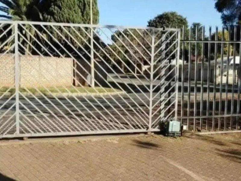 A view of the property entrance featuring a sliding security gate with an electric motor and paved driveway access.