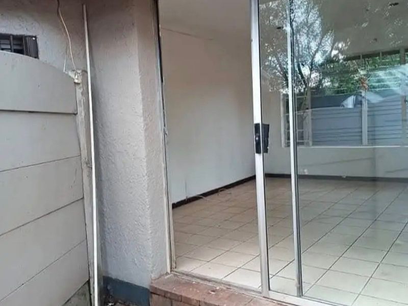 Exterior view of a patio area featuring brick paving and a sliding glass door leading into an empty tiled interior space.