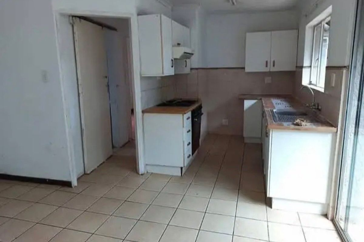 A functional, empty kitchen featuring built-in cabinetry, laminate countertops, a stainless steel sink, and integrated cooking appliances with tiled flooring.