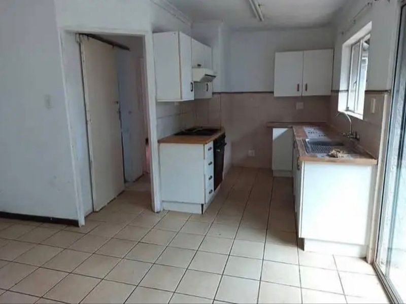 A functional, empty kitchen featuring built-in cabinetry, laminate countertops, a stainless steel sink, and integrated cooking appliances with tiled flooring.