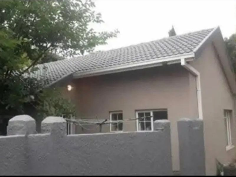 A view of the rear exterior of the house featuring a tiled roof, gutters, and a solid boundary wall.