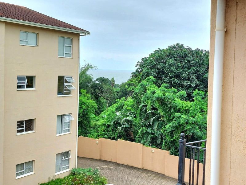 A view from the apartment overlooking the complex driveway, surrounding lush greenery, and a distant ocean horizon.