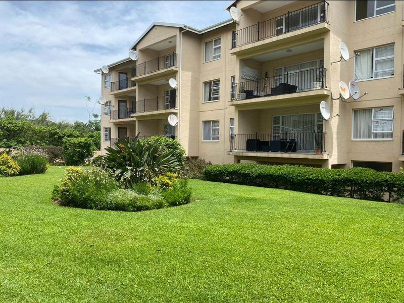 Exterior view of a multi-story apartment building featuring private balconies with metal railings, sliding glass doors, and a well-maintained communal garden area.