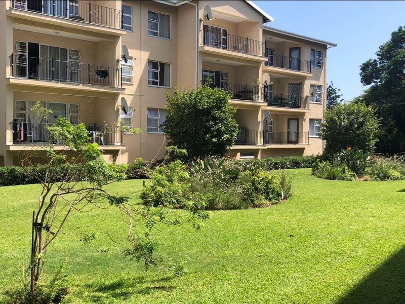 Rear view of a multi-story apartment complex featuring private balconies with metal railings overlooking a well-maintained communal garden area.