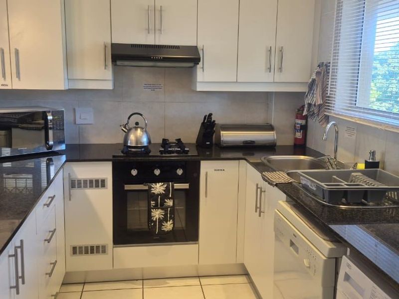 A functional kitchen featuring white cabinetry, granite countertops, a built-in oven with gas hob, and an extractor fan, complemented by tiled flooring and backsplash.