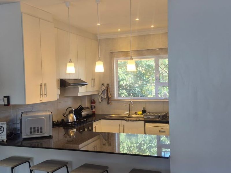 A functional kitchen featuring white cabinetry, granite countertops, a breakfast bar, and integrated appliances, illuminated by pendant and recessed lighting.