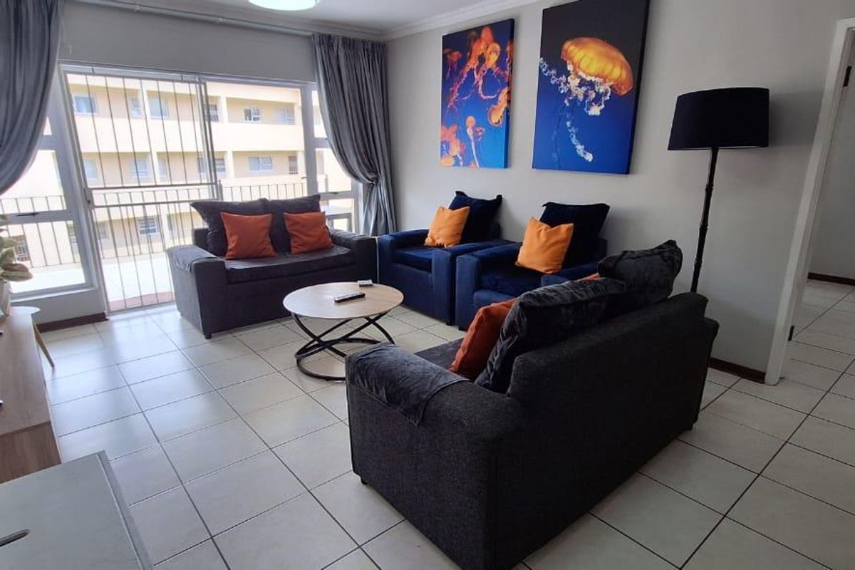 A well-lit living room featuring neutral tiled flooring and a large sliding glass door with security gate, providing access to an outdoor balcony area.