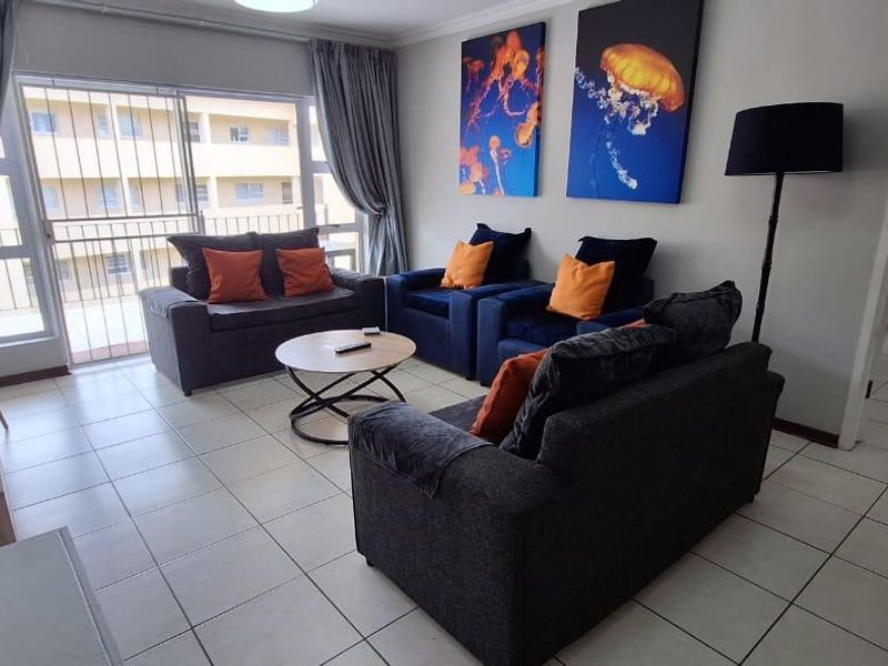 A well-lit living room featuring neutral tiled flooring and a large sliding glass door with security gate, providing access to an outdoor balcony area.