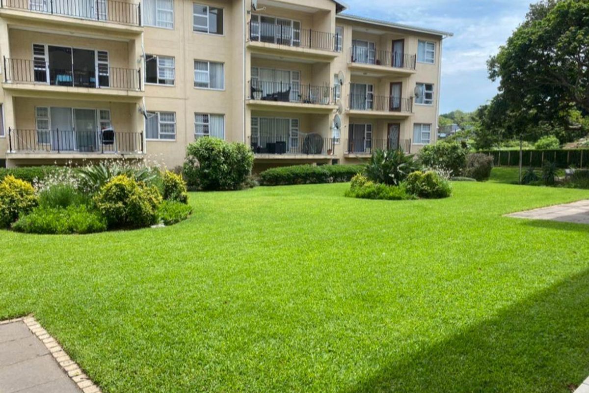 Rear view of the apartment complex featuring multiple balconies, sliding glass doors, and a well-maintained communal garden area.