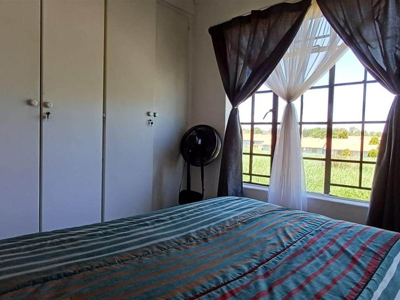 A bedroom featuring built-in cupboards and a large window with natural light, offering a view of the surrounding area.