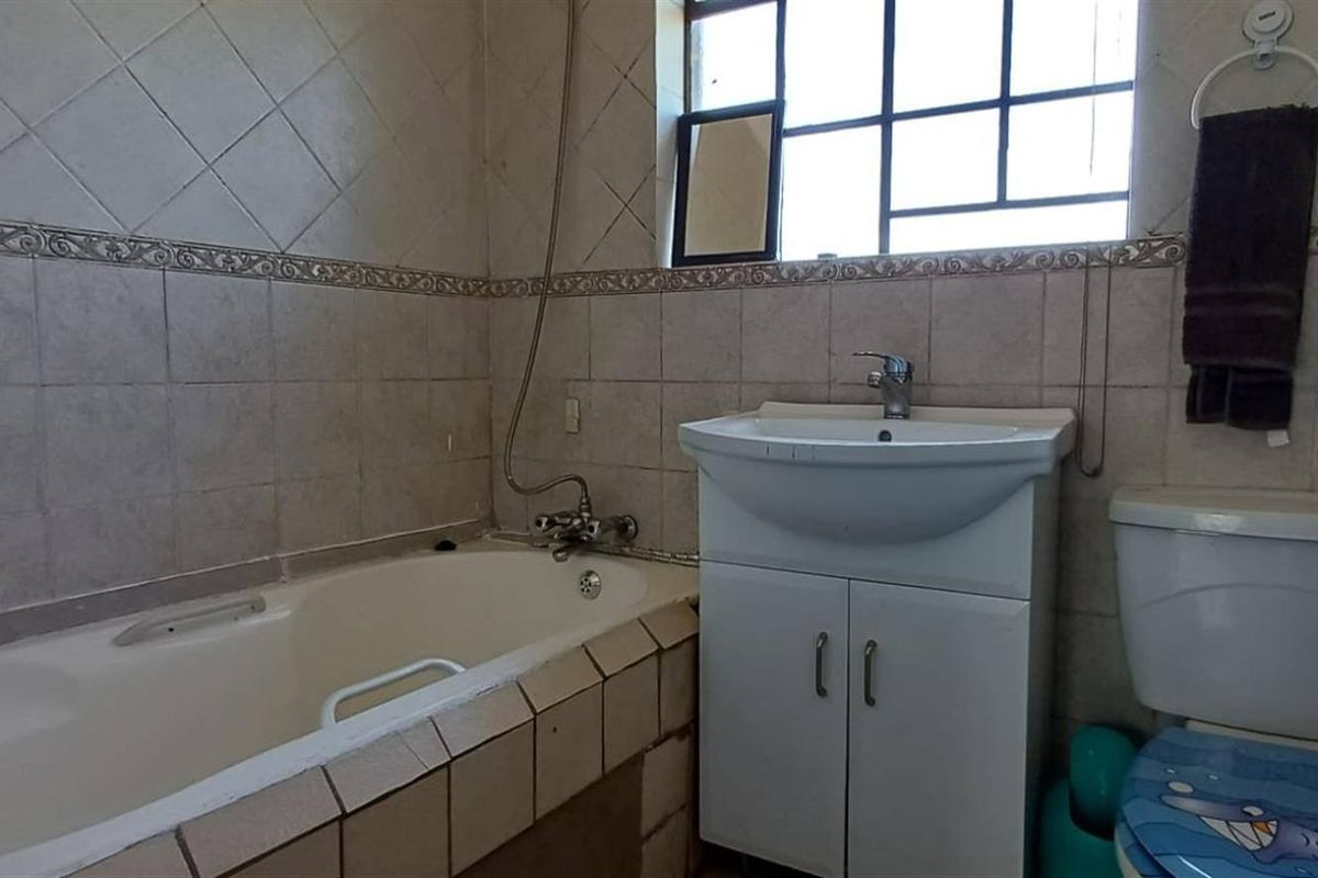 A functional bathroom featuring a bathtub, vanity basin, and toilet with tiled wall finishes and a window for natural light.