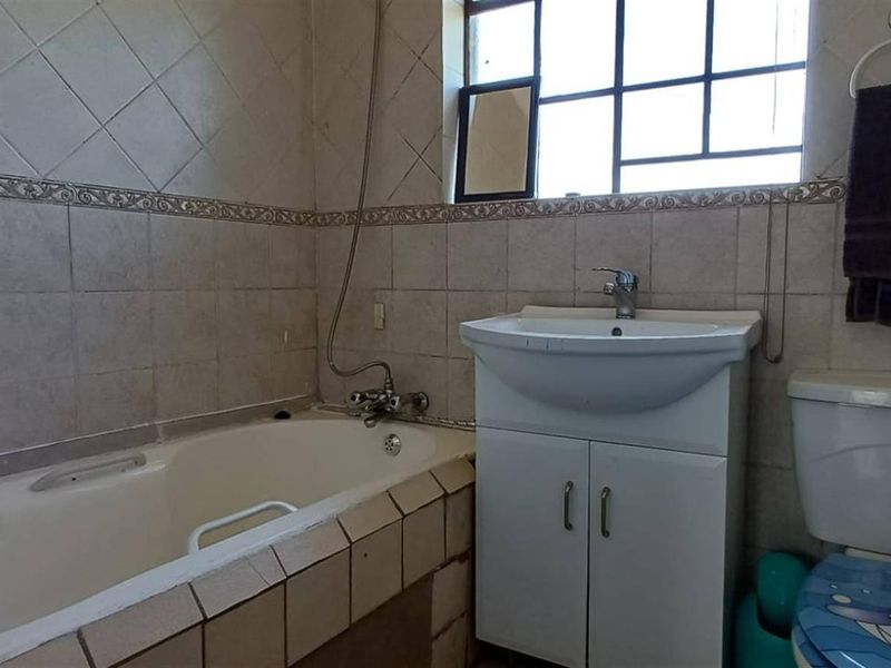 A functional bathroom featuring a bathtub, vanity basin, and toilet with tiled wall finishes and a window for natural light.